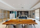 This single-floor facility at 28250 S Dixie Hwy, FL, offers a thoughtfully designed communal space with two distinct areas. The open-concept lounge and kitchen area features a striking live-edge wood dining table as its centerpiece, complemented by a modern kitchen island with bar seating. Dark cabinetry, a mosaic tile backsplash, pendant lighting, and recessed ceiling details lend a contemporary aesthetic, while large windows with roller shades allow natural light to fill the space. A vibrant teal accent door adds a pop of color to the otherwise neutral palette.

The fitness center is well-appointed and divided into dedicated zones for cardio and strength training. The cardio area includes treadmills, ellipticals, a stationary bike, and a stair climber, with direct access to the outdoors through glass double doors that provide views of the surrounding greenery and pool area. The strength training zone is equipped with multiple cable and resistance machines arranged on durable rubber flooring. Recessed lighting and windows throughout the fitness space maintain a bright, energizing environment. Together, these amenities provide a comprehensive and functional space suited for both social gatherings and active wellness routines.