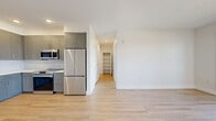 Located in Littleton, Colorado, this well-appointed one-bedroom, one-bathroom residence offers a thoughtfully designed single-floor layout. Light wood-tone flooring flows throughout the main living areas, creating a bright and cohesive aesthetic. The open-concept kitchen and living room serve as the heart of the home, with the kitchen showcasing gray shaker-style cabinetry, white quartz countertops, a subway tile backsplash, open floating shelves, and a full suite of stainless steel appliances including a French door refrigerator, electric range, built-in microwave, and dishwasher. A hallway leads from the main living area to a dedicated closet with open shelving, offering generous storage. The bedroom features plush carpeting, a ceiling fan, a large window with neighborhood views, and a sliding glass door opening to a private balcony. The full bathroom is finished with gray cabinetry, a white quartz vanity, a soaking tub with tiled surround, and brushed nickel fixtures. Clean white walls, recessed lighting, and modern hardware are consistent throughout, giving the entire space a fresh, move-in-ready feel.