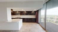 This single-floor residence offers a thoughtfully designed layout with a variety of functional and stylish spaces throughout. The kitchen is a standout feature, showcasing rich dark wood cabinetry that extends from floor to ceiling, pristine white quartz countertops, a decorative tile backsplash with a geometric gold-accent pattern, and stainless steel appliances including a range, microwave, and refrigerator. A large island provides additional prep and serving space, while floor-to-ceiling sliding glass doors flood the kitchen with natural light and open to a private balcony offering expansive outdoor views of the surrounding cityscape and greenery.

The bedrooms are generously sized, featuring plush carpeting, clean white walls, and large sliding glass doors with dark drape panels that frame scenic outdoor views. The open, airy feel of each room is enhanced by recessed lighting and ample wall space.

The bathrooms are carefully finished with mosaic tile floors and decorative accent tile walls. One bathroom features a crisp white subway-style tile tub surround with colorful vertical mosaic accents, while another showcases a bold geometric patterned wall tile in warm tones, each fitted with a combination tub and shower.

Additional areas include a versatile entry or utility room with marble-style tile flooring and a sliding door leading to adjacent spaces, completing this well-rounded and elegantly detailed residence.