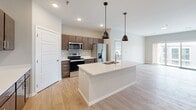 Located at 3280 Veterans Blvd S in Fargo, North Dakota, this single-floor unit offers a thoughtfully designed, contemporary layout that balances open communal spaces with well-defined private areas. The floor plan, visible in the 3D overview, reveals a logical flow between living, kitchen, and sleeping quarters.

The kitchen serves as a central hub, featuring dark espresso cabinetry, stainless steel appliances including a range, microwave, and refrigerator, and a large center island with a white quartz countertop, undermount sink, and stylish pendant lighting overhead. Light wood-style flooring extends through the kitchen and living areas, lending warmth and continuity throughout.

The living room is generously proportioned, bathed in natural light from a full sliding glass door that opens onto a private balcony with exterior views of the surrounding development. Neutral gray walls and clean white trim contribute to the bright, modern aesthetic.

Bedrooms are carpeted for comfort, each featuring windows with blinds that bring in natural light. The primary bathroom includes a wide vanity with dark cabinetry, a large mirror, tile flooring, and access to a walk-in closet area. A secondary bathroom offers a tub-shower combination, wood-style flooring, and additional cabinet storage, completing this well-appointed unit.