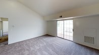 This 2-bedroom, 1-bathroom apartment is thoughtfully laid out across a single floor, offering a comfortable and functional living environment. The open living area features soft wall-to-wall carpeting and vaulted ceilings that lend a sense of spaciousness, with a sliding glass door that floods the room with natural light and provides direct access to an outdoor space. The kitchen is well-appointed with white cabinetry, granite-style countertops, a mosaic tile backsplash, and a full suite of white appliances including a dishwasher, electric range, and over-the-range microwave. Light tile flooring completes the kitchen's clean, bright aesthetic. The two bedrooms are carpeted and neutrally finished, offering versatile spaces suitable for a variety of arrangements; one bedroom features a window with outdoor views, while the other is a quiet, enclosed retreat. The bathroom is clean and efficiently designed, featuring a full tub-shower combination, a toilet, and a vanity topped with granite-style countertops and a mirrored medicine cabinet. Neutral tones throughout the unit create a cohesive, move-in-ready atmosphere that is both practical and inviting.