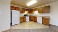 Located at 14320 Dysprosium St NW in Ramsey, Minnesota, this single-floor unit offers a functional and straightforward layout designed for comfortable everyday living. The kitchen is a standout feature, showcasing warm oak cabinetry that extends across the walls in an L-shaped configuration, offering generous storage both above and below the counter. Neutral laminate countertops provide ample workspace, and the kitchen is equipped with a white refrigerator, electric range, dishwasher, and a double-basin sink. Light tile flooring runs throughout the kitchen, adding to its clean, practical aesthetic. The living area is carpeted and filled with natural light, courtesy of a large sliding glass door that opens to an outdoor view of lush greenery. A wall-mounted air conditioning unit and baseboard heating ensure year-round comfort. The bedroom is similarly carpeted, featuring baseboard heating and easy access to the hallway and closet. The bathroom is generously sized, with oak vanity cabinetry, tile flooring, and safety grab bars, reflecting a thoughtful and accessible design. The overall ambiance of the space is warm and understated, with neutral tones and practical finishes throughout.