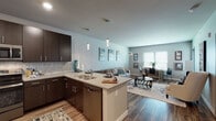 This single-floor residence offers a thoughtfully designed open-concept layout that seamlessly connects the kitchen, dining, and living areas. The kitchen is a standout feature, showcasing rich dark espresso cabinetry, light quartz countertops, a tile mosaic backsplash, and a full suite of stainless steel appliances. A peninsula with an extended breakfast bar provides additional seating and serves as a natural divider between the kitchen and living space. Elegant pendant lighting illuminates the prep area, adding a contemporary touch.

The living area benefits from multiple windows dressed with horizontal blinds, allowing generous natural light to fill the space. Wood-style flooring runs throughout the main living areas, lending warmth and continuity, while plush carpet transitions into the bedroom.

The bedroom is a comfortable retreat, featuring a ceiling fan, a large window with outdoor views, and ample room for furnishings. The bathroom includes a dual-sink vanity with dark cabinetry, a wide mirror, and a full tub-shower combination. Neutral tones and consistent modern finishes create a cohesive aesthetic throughout the entire residence.