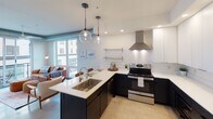 Located at 1439 W Lake St in the vibrant Uptown neighborhood of Minneapolis, this modern single-floor unit offers a thoughtfully designed open-concept layout with clean, contemporary finishes. The living area is bathed in natural light through expansive floor-to-ceiling windows and sliding glass doors that open onto a private balcony, offering views of the surrounding cityscape. Exposed industrial-style ductwork adds an urban character to the space, complemented by polished concrete floors that extend throughout.

The kitchen is a standout feature, boasting sleek two-tone cabinetry with dark lower cabinets and white uppers, white quartz countertops, stainless steel appliances including a range with a wall-mounted hood, and a peninsula with pendant globe lighting — ideal for both cooking and casual dining.

Two bedrooms provide comfortable retreats; one enjoys direct balcony access through large glass doors with the same industrial ductwork detail, while the second offers a quieter, cozier atmosphere with neutral tones.

The unit includes two bathrooms: one with a soaking tub and dark vanity cabinetry, and another featuring a glass-enclosed walk-in shower. Together, the spaces deliver a cohesive, modern aesthetic well-suited for urban living in Minneapolis.