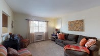 This single-floor residence offers a thoughtfully laid-out living space designed for everyday comfort and functionality. The living room serves as a welcoming gathering area, featuring carpet flooring, a large window with sheer curtains that invite natural light, and a spacious closet for added storage. The adjacent dining area accommodates a full-sized dining table with seating for several guests, illuminated by a central pendant light fixture. The kitchen is well-equipped with rich dark wood cabinetry, granite-style countertops, a gas range, dishwasher, and a double-basin sink, all complemented by hardwood-style flooring and natural light from dual windows. The primary bedroom is generously sized with carpet flooring, dual windows offering natural light, and ample room for a full furniture arrangement. A second bedroom provides comfortable accommodations with carpet flooring and a window. The bathroom features hardwood-style flooring, a vanity with storage, and baseboard heating. A dedicated in-unit laundry room with a full-size washer and dryer, topped by wood cabinetry, adds significant everyday convenience. Throughout, neutral wall tones and consistent finishes create a cohesive and functional living environment.