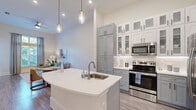 Located at 1231 Arya Way in Ocoee, FL, this well-appointed 1-bedroom, 1-bathroom home offers a thoughtfully designed open-concept layout across a single floor. The combined living, dining, and kitchen area serves as the heart of the home, highlighted by soaring ceilings and large windows that flood the space with natural light. The kitchen is a standout feature, boasting a curved white quartz island with a built-in sink, two-tone gray and white shaker cabinetry with glass-front upper panels, white subway tile backsplash, and a full suite of stainless steel appliances including a side-by-side refrigerator with water dispenser, range, microwave, and dishwasher. Elegant pendant lighting completes the look. The living area features impressively tall ceilings and floor-to-ceiling windows with access to the patio, creating an airy, open ambiance. Light wood-tone flooring runs throughout. The bedroom is a serene retreat with high ceilings, large windows offering outdoor views, and two closets for ample storage. The bathroom features a gray vanity with dual sinks, large-format tile flooring, and a glass-enclosed shower. A dedicated laundry room houses a full-size washer and dryer with overhead cabinetry. A private patio completes this home.