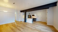This single-floor unit showcases a thoughtful blend of industrial architectural elements and modern design. The open-concept living and kitchen area is anchored by bold dark structural beams and columns that contrast sharply against white walls and ceilings, creating a striking visual character throughout. Light hardwood flooring runs continuously across the space, enhancing the sense of openness and warmth.

The kitchen is well-appointed with dark wood cabinetry, white upper cabinets, a classic subway tile backsplash, and a full suite of stainless steel appliances including a refrigerator, range, and built-in microwave. A generously sized island with a dramatic veined white stone countertop serves as a functional centerpiece and natural divider between the kitchen and living areas.

The bedrooms are bright and airy, each featuring large multi-pane windows that invite natural light and offer views of the surrounding neighborhood. The rooms are finished with the same hardwood flooring and clean white walls, providing a versatile, neutral backdrop.

Two bathrooms serve the unit: one features large-format neutral tile and a glass-enclosed walk-in shower, while the other offers a clean, minimalist design with a floating vanity and tiled flooring. Together, these spaces reflect a cohesive, contemporary aesthetic throughout.