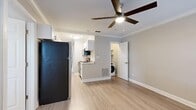 This single-floor unit offers a clean, modern aesthetic throughout, unified by light wood-style flooring that flows seamlessly across all living areas. The open kitchen is a functional highlight, featuring white shaker cabinets, granite countertops, stainless steel appliances including a range, microwave, and refrigerator, and a sink positioned along a peninsula that connects to the main living area. Crown molding and a ceiling fan with built-in lighting add a polished touch to the living space, which also benefits from natural light filtering in through blinded windows. A dedicated alcove off the living area conveniently houses an in-unit washer, adding everyday practicality. The unit includes multiple bedrooms, each finished with the same light flooring, ceiling fans, and windows dressed with white blinds that allow for natural light while maintaining privacy. One bedroom features a walk-in closet, providing generous storage. The bathrooms are finished with full-height neutral ceramic tile surrounds enclosing soaking tubs with shower combinations, complemented by clean white fixtures throughout. The overall palette of soft grays and whites creates a bright, neutral atmosphere well-suited for comfortable everyday living.