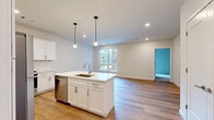 Located at 141 Danbury Rd in Wilton, CT, this thoughtfully designed single-floor unit offers a bright, modern living experience across a well-utilized floor plan. The open-concept kitchen serves as the centerpiece of the main living area, featuring white shaker cabinetry, subway tile backsplash, sleek white countertops, and a central island with a stainless steel sink and pendant lighting overhead. Stainless steel appliances, including a refrigerator, range, microwave, and dishwasher, complete the kitchen's contemporary finish. Light hardwood-style flooring flows throughout the main living areas, enhancing the sense of openness and warmth, while large windows allow natural light to fill the space. The bedroom is finished with plush carpeting and provides access to a spacious walk-in closet equipped with wire shelving and hanging rods for ample storage. An additional room with hardwood-style flooring offers flexible use as a secondary bedroom or office, also benefiting from natural light through its windows. The bathroom is finished with large-format white tile flooring, a white vanity with backlit mirror, and a tub-shower combination with vertical subway tile surround, maintaining the unit's clean, contemporary aesthetic throughout.