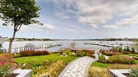 Located along the scenic Navesink River in Red Bank, NJ, this meticulously landscaped waterfront property at 122 Bodman Place offers a stunning outdoor environment designed for both relaxation and enjoyment of its natural surroundings. A signature herringbone-patterned paver walkway winds gracefully through the grounds, connecting multiple distinct seating and recreation areas across the well-maintained lawn. Lush, layered garden beds feature ornamental grasses, flowering perennials, hydrangeas, and seasonal plantings that provide year-round color and texture. A spacious composite deck with sleek cable railing sits directly at the water's edge, offering unobstructed panoramic views of the Navesink River and the neighboring marina, where boats are docked at multiple piers. Several intimate outdoor seating areas are thoughtfully integrated into the landscape, inviting residents to take in the waterfront scenery. Mature trees provide natural shade and visual anchoring throughout the grounds. The property also includes a gently graded lawn area ideal for casual outdoor gatherings, bordered by curved garden beds and connected via stone-paved pathways. The overall ambiance is that of a serene, resort-inspired waterfront retreat, combining refined landscaping with direct access to one of Red Bank's most coveted natural assets.