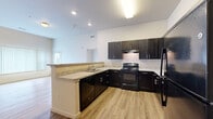 This well-appointed single-story residence offers four bedrooms and two full bathrooms within a thoughtfully designed floor plan. The open-concept kitchen and living area serves as the heart of the home, featuring striking dark espresso cabinetry, light granite-style countertops, a peninsula with a sink, and black appliances including a range and refrigerator. Warm wood-look luxury vinyl flooring runs throughout the main living areas, creating a cohesive and easy-to-maintain finish. The living room receives natural light through a windowed exterior door, lending the space a bright and airy atmosphere. Each bedroom is finished with plush wall-to-wall carpeting and vertical blinds, providing comfort and privacy. The primary bedroom includes access to a dedicated closet with built-in wire shelving, while a second closet offers additional storage. The bathrooms are finished with matching dark cabinetry, granite-style countertops, wood-look flooring, and well-lit vanity mirrors. One bathroom features a clean, all-white walk-in shower unit with built-in corner shelving. Neutral wall tones and consistent finishes throughout lend the home a cohesive, move-in-ready feel.