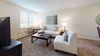 185 Ludlow is a thoughtfully designed single-floor residence that offers a comfortable and functional layout across several distinct living areas. The living room serves as the heart of the home, featuring neutral-toned walls, plush carpeting, and large windows that welcome an abundance of natural light. The space comfortably accommodates a seating arrangement and provides a warm, inviting ambiance. Adjacent to the living area, a dedicated dining space offers room for a full dining set, accented by soft wall tones and carpeted flooring that carry throughout the home. The kitchen is efficiently laid out with ample white cabinetry, generous counter space, and essential appliances including a range, making it well-equipped for everyday cooking. The bedrooms are generously sized, each with carpeted floors, windows with blinds, and ample room for furnishings. The primary bedroom benefits from direct access to a bathroom featuring a vanity with lighted mirror and a full soaking tub with clean white tile surround. Throughout the residence, the neutral color palette, consistent flooring, and practical design choices come together to create a cohesive and comfortable living environment.