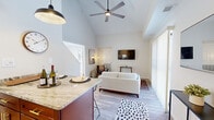 TRELLIS Herndon Unit 3 is a two-story, two-bedroom, one-bathroom residence in Herndon, Virginia, thoughtfully designed to maximize comfort and functionality across two well-proportioned floors. The main level hosts the kitchen and living area beneath striking vaulted ceilings, creating an airy, open atmosphere. The kitchen features white cabinetry with gold hardware, stainless steel appliances, and a granite-topped island with bar seating, illuminated by pendant lighting. It flows seamlessly into the living area, where large sliding glass doors flood the space with natural light and provide outdoor views. A ceiling fan anchors the soaring ceiling above. Light wood-tone flooring runs throughout both levels, lending a cohesive, modern feel. The upper floor contains both bedrooms and the shared bathroom. The generously sized primary bedroom offers ample space and natural light, while the second bedroom features a bright window and closet. The full bathroom is finished with large-format tile surrounding a soaking tub and shower combination, complemented by brushed gold fixtures. Throughout, the clean, neutral palette and contemporary finishes create a bright, welcoming ambiance.