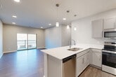 This well-appointed 2-bedroom, 2-bathroom residence in Bellevue, Nebraska offers a thoughtfully designed single-level layout with a clean, modern aesthetic throughout. The open-concept living area anchors the home, seamlessly connecting the kitchen, dining, and living spaces under recessed lighting and wood-style flooring that extends throughout the main areas. The kitchen is a standout feature, boasting a large center island with a built-in sink and white quartz countertops, gray shaker-style cabinetry, and a full suite of stainless steel appliances including a refrigerator, range, microwave, and dishwasher. Pendant lighting above the island adds a polished finishing touch. The living area is bright and open, with sliding glass doors leading to a private patio that overlooks a natural outdoor setting. Both bedrooms offer plush carpet flooring and generous closet space, with the primary bedroom featuring its own en-suite bathroom equipped with a wide vanity and a walk-in closet. The second bathroom mirrors the same refined finishes. Additional highlights include a dedicated laundry area, multiple closets for ample storage, and a hallway connecting the private quarters. The overall ambiance is fresh, neutral, and move-in ready.