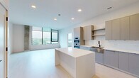 Located on the 15th floor at 2901 Crystal Dr in Arlington, Virginia, this thoughtfully designed 2-bedroom, 3-bathroom residence offers a sleek, contemporary living experience across a well-appointed single floor. The open-concept kitchen and living area serves as the heart of the home, featuring a large central island with a crisp white countertop, flat-front cabinetry in warm neutral tones, stainless steel double wall ovens, a gas cooktop with a stainless range hood, and a black-accented undermount sink. Light hardwood flooring extends throughout, complementing the clean, minimalist aesthetic. Floor-to-ceiling windows in the living area and both bedrooms flood the space with natural light while framing expansive views of the Arlington skyline and surrounding tree canopy. The primary bedroom is generously proportioned and features exposed concrete column accents that add an industrial-modern character. Both bedrooms benefit from dedicated closets with built-in shelving systems for efficient storage. The three bathrooms are finished with large-format tile flooring and modern fixtures with matte black hardware accents. An in-unit laundry area houses a stacked full-size washer and dryer, adding everyday convenience. The overall ambiance is bright, airy, and refined, with a consistent modern design language throughout.
