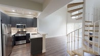 Located at 7137 Alvern St in Los Angeles, CA, this two-story residence offers a well-designed layout across two distinct levels connected by a distinctive carpeted spiral staircase. The main level features rich hardwood flooring throughout, anchored by a living area with soaring ceilings and a built-in fireplace. Vertical blinds along the living room wall allow for natural light control while framing views of the surrounding greenery.

The kitchen is outfitted with dark, textured cabinetry paired with bright white quartz countertops and a decorative tile backsplash in neutral tones. Stainless steel appliances, including a gas range, built-in microwave, and refrigerator, complete the space. A peninsula with an integrated sink adds additional prep and seating space, creating a seamless connection between the kitchen and living areas.

The bathroom features dark wood vanity cabinetry, a quartz countertop with an undermount sink, a framed mirror, and a combined tub and shower. Hardwood flooring extends into this space as well.

Upstairs, the loft-style upper level showcases vaulted ceilings, a small window overlooking tree canopy, and soft carpeting underfoot, creating a bright and airy retreat. The upper level overlooks the main floor, reinforcing the open, expansive feel of the home.