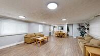 Located at 5220 Luzzane Dr in Indianapolis, IN, this single-floor community space offers a well-organized layout designed for both relaxation and activity. The main gathering area is expansive and open, featuring durable wood-look flooring, neutral gray walls, and multiple flush-mount ceiling light fixtures that provide consistent, even illumination throughout. Large windows fitted with blinds allow natural light to filter into the space while maintaining privacy.

The lounge area is furnished with comfortable seating, coffee tables, and side tables, while decorative potted plants and framed artwork add warmth to the environment. Adjacent to the lounge, a dining area accommodates a full table and chair set, making it well-suited for communal meals or group meetings. A mirror and framed art on the walls enhance the sense of openness in this section.

A compact kitchenette is equipped with white cabinetry, a stainless steel sink, countertop space, a microwave, and a dishwasher — providing convenient food preparation and clean-up capabilities. The exercise room is outfitted with multiple cardio machines, including treadmills and other fitness equipment, offering a dedicated space for physical wellness. Throughout the space, the clean, functional design and cohesive aesthetic make it a practical and welcoming environment for community use.