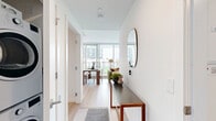 Located on Ash Street in Vancouver, BC, this well-appointed 2-bedroom, 3-bathroom residence offers a thoughtfully designed open-concept layout with clean, modern finishes throughout. Light hardwood flooring extends across the living areas, complementing the crisp white walls and creating a bright, cohesive aesthetic.

The entry hallway welcomes residents with a sleek console and mirror, leading into the combined living, dining, and kitchen area. Floor-to-ceiling windows flood the main living space with natural light and provide direct access to a private balcony with urban views. The kitchen features light wood cabinetry, white quartz countertops, stainless steel appliances including a full-size refrigerator and range, and a clean tile backsplash — balancing style with functionality.

Both bedrooms are well-proportioned and bright, with large windows overlooking the surrounding neighbourhood's greenery. Each room includes dedicated closet space, and the second bedroom is well-suited as a home office. The three bathrooms are finished in clean white tile with tub-and-shower combinations. Additional conveniences include in-unit laundry, multiple closets, and a hallway connecting the private quarters from the main living areas, ensuring a practical and comfortable flow throughout.