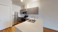This 2-bedroom, 1-bathroom residence at 6035 Park Ave in West New York, NJ offers a clean, modern aesthetic throughout its single-floor layout. Warm hardwood flooring extends across the living areas and bedrooms, creating a cohesive and inviting atmosphere. The open-concept living area is bright and spacious, with a window allowing natural light to fill the room. The kitchen is thoughtfully designed with contemporary taupe cabinetry, white countertops, a stainless steel sink, and a full suite of stainless steel appliances including a refrigerator, electric range, and over-the-range microwave. A peninsula counter provides additional workspace and a natural transition between the kitchen and living area. The bathroom features tile flooring in a light wood-look finish, a vanity with matching cabinetry, and wall-mounted storage, offering both style and practicality. A generously sized walk-in closet with multi-tier wire shelving provides abundant storage. The unit's neutral white walls and consistent flooring throughout give the space a fresh, move-in-ready feel well-suited for comfortable urban living.