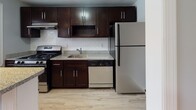 Located at 81 Hammell Place in Maywood, NJ, this single-floor unit offers a well-organized layout with consistent design choices throughout. Warm-toned hardwood flooring extends across the living areas and bedrooms, complemented by soft blue-gray walls and crisp white trim that create a calm, cohesive atmosphere.

The open living area is bright and welcoming, featuring recessed lighting, two windows that bring in natural light, and a staircase with white-painted balusters adding architectural character. A ceiling fan with integrated lighting is installed in one of the bedrooms, which also benefits from dual windows and a radiator for heating. Additional rooms share the same hardwood floors and neutral tones, offering flexibility in use.

The kitchen is outfitted with rich dark-wood cabinetry, granite-style countertops, a white subway tile backsplash, and stainless steel appliances including a gas range and refrigerator, alongside a dishwasher. Light wood-look flooring grounds the kitchen space.

The bathroom features a full tub-shower combo enclosed in white subway tile, a dark vanity with granite-style countertop, light tile flooring, and a small window for natural ventilation. The overall space is practical, well-maintained, and move-in ready.