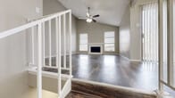 This two-floor home offers a thoughtfully designed layout that balances open communal living with comfortable private spaces. The main living area immediately impresses with its soaring vaulted ceiling, anchored by a ceiling fan with light kit and a classic fireplace framed by multiple windows dressed with blinds that invite natural light. Rich, dark hardwood-style flooring flows throughout the main living space, adding warmth and visual depth.

A white-railed staircase connects both levels, adding an architectural element that enhances the home's open feel. The kitchen is a functional galley-style space featuring dark espresso cabinetry on both sides, light speckled countertops, a mosaic tile backsplash, a double sink, and white appliances including a range and refrigerator. A peninsula with wainscoting detail separates the kitchen from the adjoining dining area, which is accented by an elegant chandelier.

The bedrooms are generously sized, each with plush carpeting, ceiling fans, and ample closet space. One bedroom features sliding glass door access to an outdoor space. Bathrooms are finished with dark vanity cabinetry, light countertops, large mirrors, and wood-style flooring. The textured ceilings and neutral warm-gray wall tones throughout create a cohesive and inviting ambiance across all areas of the home.