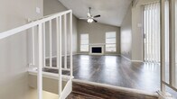 This two-floor home offers a thoughtfully designed layout that balances open communal living with comfortable private spaces. The main living area immediately impresses with its soaring vaulted ceiling, anchored by a ceiling fan with light kit and a classic fireplace framed by multiple windows dressed with blinds that invite natural light. Rich, dark hardwood-style flooring flows throughout the main living space, adding warmth and visual depth.

A white-railed staircase connects both levels, adding an architectural element that enhances the home's open feel. The kitchen is a functional galley-style space featuring dark espresso cabinetry on both sides, light speckled countertops, a mosaic tile backsplash, a double sink, and white appliances including a range and refrigerator. A peninsula with wainscoting detail separates the kitchen from the adjoining dining area, which is accented by an elegant chandelier.

The bedrooms are generously sized, each with plush carpeting, ceiling fans, and ample closet space. One bedroom features sliding glass door access to an outdoor space. Bathrooms are finished with dark vanity cabinetry, light countertops, large mirrors, and wood-style flooring. The textured ceilings and neutral warm-gray wall tones throughout create a cohesive and inviting ambiance across all areas of the home.