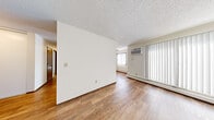 This single-floor unit offers a clean, functional layout designed for comfortable everyday living. The living area is bright and open, featuring warm wood-look laminate flooring, neutral white walls, and a textured ceiling. Large windows dressed with vertical blinds allow natural light to fill the space, while a wall-mounted air conditioning unit and baseboard heaters ensure year-round climate control.

The galley-style kitchen is efficiently designed with white shaker cabinetry, light countertops, a stainless steel sink, and a full suite of stainless steel appliances including an electric range, microwave, and refrigerator. A ceiling fan with a light fixture provides additional ventilation, and a window with vertical blinds brings in natural light.

The bedrooms are carpeted for comfort and include ceiling fans. The primary bedroom features access to a walk-in closet and a private door to the bathroom, offering added convenience. An additional room with matching carpet and a neutral palette provides flexible use as a second bedroom or den.

The bathroom includes a white vanity with a single basin sink, light countertop, and a mirrored medicine cabinet above. Dark wood-toned doors and trim throughout add a warm contrast to the predominantly white interior, giving the space a cohesive and tidy overall aesthetic.