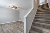 This two-story home offers four bedrooms and one bathroom distributed across two thoughtfully laid-out floors. The main level features light wood laminate flooring throughout the living area and kitchen, lending a bright, clean aesthetic to the space. A ceiling fan with a built-in light fixture adds a practical touch to the living area, which is connected to the upper level via a carpeted staircase with a clean white banister.

The kitchen is well-appointed with warm oak wood cabinetry, white countertops, and a full suite of white appliances including a refrigerator, electric range, dishwasher, and double-basin sink. A window above the sink allows natural light to fill the space, and durable wood laminate flooring carries through from the adjacent living area.

The bedrooms are located on both floors and feature plush neutral carpet, ample natural light from large windows, and individual closets with built-in shelving and hanging rods. The spacious primary bedroom includes its own dedicated closet.

The bathroom is clean and functional, featuring a single-sink vanity with dark cabinetry, a toilet, and a full tub-shower combo with white surround. Hallways connect each room efficiently across both floors, contributing to a practical and navigable floor plan throughout the home.