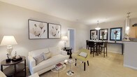 This contemporary apartment showcases a thoughtfully designed layout that maximizes space and functionality. The heart of the home is an open-concept living and dining area, adorned with elegant furnishings and tasteful artwork. The living room features a plush white sofa, complemented by a pale yellow accent chair and modern coffee tables. Large floral prints add a touch of sophistication to the space.

The adjacent dining area boasts a glass table with sleek chairs, while a console table with decorative vases adds visual interest. The kitchen is equipped with wooden cabinetry, black appliances, and ample counter space, perfect for culinary enthusiasts.

The bedrooms are havens of comfort, with one featuring a king-size bed adorned with a striking yellow headboard and crisp white linens. Another bedroom showcases a queen-size bed with a dark wooden frame and neutral bedding. Both rooms have windows allowing natural light to flood in.

The bathroom is functional and stylish, with a single vanity, large mirror, and a shower/tub combination. A separate laundry room with full-size washer and dryer adds convenience. The apartment also includes a walk-in closet with built-in shelving for organized storage.

Throughout the space, neutral tones create a calm ambiance, while carefully chosen accents add pops of color and personality. The overall design aesthetic is clean, modern, and inviting, perfect for contemporary living.