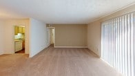 This single-floor unit offers a straightforward, functional layout spread across multiple rooms, as illustrated by the 3D floor plan model. The living area is generously sized, featuring neutral-toned carpet, a textured ceiling, and a sliding glass door that introduces natural light. An adjacent dining area is distinguished by a brass candelabra-style chandelier, adding a classic touch to the otherwise understated space.

The kitchen is equipped with light wood cabinetry, laminate countertops, and a white electric range with an overhead exhaust fan, providing a practical cooking environment. The layout connects efficiently to the rest of the unit.

The bedrooms are carpeted and bright, each featuring windows with blinds that allow natural light to filter in. The primary bedroom includes direct access to a private bathroom fitted with a vanity, mirror, and ample counter space.

Two full bathrooms serve the unit, both featuring tub-shower combinations with beige subway tile surrounds, toilets, and wall-mounted mirrors. Textured ceilings are consistent throughout the unit, and neutral wall tones create a cohesive, clean aesthetic across all spaces.