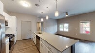 This contemporary single-floor residence offers a thoughtfully designed open-concept layout that seamlessly connects the kitchen, dining, and living areas. The kitchen is a standout feature, showcasing a large center island with quartz countertops, a stainless steel sink, and a full suite of stainless steel appliances including a French door refrigerator, gas range, built-in microwave, and dishwasher. Crisp white cabinetry with brushed hardware pairs with a herringbone tile backsplash to create a clean, modern aesthetic, while pendant lighting above the island adds a warm, inviting touch. Wood-look plank flooring flows throughout the main living areas, anchoring the open layout. The spacious living room benefits from multiple windows and a sliding door that invite natural light and outdoor views, complemented by a ceiling fan for added comfort. Bedrooms are carpeted and finished with neutral tones, each featuring windows and ceiling fans. The primary bathroom is appointed with a dual-sink vanity, quartz countertops, white cabinetry, and a walk-in glass-enclosed shower with floor-to-ceiling tile. A secondary bathroom offers a single vanity with matching finishes. The overall design is clean, modern, and move-in ready.