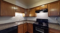 Located at 4653 Refugee Rd in Columbus, Ohio, this single-floor unit offers a practical and well-appointed layout with consistent design elements throughout. Rich, dark wood-look flooring runs throughout the living areas and bedrooms, providing a warm and cohesive aesthetic.

The kitchen is efficiently designed in an L-shaped configuration, featuring warm-toned wooden cabinetry with ample upper and lower storage, dark granite-style countertops, a stainless steel sink, and a full suite of black appliances including an electric range with overhead ventilation hood and a dishwasher. The open sightline from the kitchen connects seamlessly to the living area, which benefits from natural light through a window overlooking greenery outside.

The living area also includes a built-in closet with a sliding door, adding convenient storage. One of the rooms features a distinctive vertical shiplap accent wall, lending a touch of modern farmhouse character. Additional rooms are bright and airy, each with windows that allow natural light in and feature the same wood-look flooring and neutral gray walls.

The bathroom includes a full tub-shower combination with a white surround, a dark-vanity with a white countertop, and wood-look flooring that ties into the rest of the unit. Overall, the space presents a clean, functional, and inviting environment suitable for comfortable everyday living.