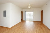 This single-floor unit is finished with warm-toned light wood flooring that runs consistently throughout every room, creating a cohesive and inviting aesthetic. The open-concept living area is bright and spacious, benefiting from natural light admitted through a sliding glass door that opens to an outdoor area. A ceiling fan overhead adds practical comfort to the living space, which flows naturally toward the kitchen.

The kitchen is well-appointed with warm oak cabinetry—both upper and lower—complemented by a neutral countertop, a stainless steel sink, and a full suite of white appliances including a range, over-the-range microwave, refrigerator, and dishwasher. An adjacent utility area houses a stacked washer and dryer, providing convenient in-unit laundry access.

The unit includes two bathrooms. The full bathroom features a vanity with medium-toned wood cabinetry, a white countertop, and a tub/shower combination with a curtain. The second bathroom offers a similar vanity setup alongside a toilet, finished with the same light wood flooring. Both bedrooms are generously sized, finished in clean white walls, and feature ceiling fans or windows that allow natural light to enter.
