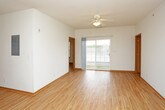 This single-floor unit is finished with warm-toned light wood flooring that runs consistently throughout every room, creating a cohesive and inviting aesthetic. The open-concept living area is bright and spacious, benefiting from natural light admitted through a sliding glass door that opens to an outdoor area. A ceiling fan overhead adds practical comfort to the living space, which flows naturally toward the kitchen.

The kitchen is well-appointed with warm oak cabinetry—both upper and lower—complemented by a neutral countertop, a stainless steel sink, and a full suite of white appliances including a range, over-the-range microwave, refrigerator, and dishwasher. An adjacent utility area houses a stacked washer and dryer, providing convenient in-unit laundry access.

The unit includes two bathrooms. The full bathroom features a vanity with medium-toned wood cabinetry, a white countertop, and a tub/shower combination with a curtain. The second bathroom offers a similar vanity setup alongside a toilet, finished with the same light wood flooring. Both bedrooms are generously sized, finished in clean white walls, and feature ceiling fans or windows that allow natural light to enter.
