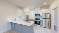 This well-designed three-story home offers 3 bedrooms and 5 bathrooms across thoughtfully arranged floors, providing ample space and functionality for everyday living. The ground floor includes an attached garage with an automatic opener, offering secure and convenient parking. Connecting hallways with light wood-style flooring guide residents through each level via carpeted staircases.

The main living floor features an open-concept kitchen and living area. The kitchen is appointed with white upper cabinetry, blue-grey lower cabinets, a white quartz peninsula with an undermount sink, stainless steel appliances including a range, microwave, and refrigerator, and light wood-style flooring. The adjacent living space is bright and airy, with recessed lighting, a wall-mounted mini-split unit, and sliding glass doors that open to a private balcony.

The upper floor is home to the bedrooms, including a generously sized primary suite with its own en-suite bathroom featuring a dual-sink vanity with grey cabinetry, white countertops, and a large mirror. Additional bedrooms are carpeted and bathed in natural light from multiple windows, with built-in closets providing practical storage. The five bathrooms throughout are clean and modern, with frosted windows for privacy. Recessed lighting and a neutral color palette create a cohesive, contemporary ambiance across all levels.