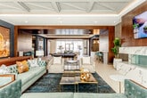 Located at 4401 Wornall Rd in Kansas City, Missouri, this single-floor amenity space offers a thoughtfully curated environment that blends elegance with functionality. The grand lounge area immediately impresses with its striking coffered ceiling detailed with geometric molding and subtle gold accents, complemented by an abundance of natural light streaming through floor-to-ceiling sheer-draped windows. Tufted sofas in rich teal and charcoal tones, layered over a deep blue patterned area rug, create an inviting and sophisticated seating arrangement, while curated artwork and gold decorative accents add warmth throughout.

The gourmet kitchen is a standout feature, appointed with high-gloss taupe cabinetry, a bold geometric mosaic tile backsplash, and a generous waterfall-edge marble island with seating for multiple guests. Professional-grade stainless steel appliances, including a large French door refrigerator and commercial-style range, make this kitchen as functional as it is visually impressive.

The game and entertainment zone features rich dark wood ceiling panels, a full-size billiards table set atop a textured area rug, a built-in bar with marble countertops and teal stools, and a wall-mounted display screen. The welcoming entry foyer continues the refined aesthetic with large-format tile flooring, a coffered ceiling, and direct access to the outdoors through full-height glass doors.