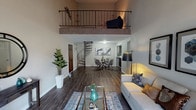 This distinctive residence on Royal Carriage Way in South Bend, Indiana, offers a thoughtfully designed loft-style layout that maximizes both functionality and visual interest. The main living area immediately impresses with its double-height ceiling and an ornamental iron-railed loft overhead, accessible via a striking spiral staircase that serves as a architectural focal point. Rich, dark hardwood-style flooring flows throughout the open-plan living and dining areas, creating a cohesive and contemporary aesthetic.

The living room provides generous space for seating and entertaining, while the adjacent dining area accommodates a round glass-topped table beneath wall-mounted artwork. The kitchen features dark wood cabinetry, white countertops, a stainless steel sink, and a dishwasher, offering a clean, modern workspace.

The bedrooms are carpeted for comfort and include natural light from well-placed windows. One bedroom features a bifold closet with built-in shelving, while another presents a more expansive layout with coordinating furnishings. The bathroom is finished with dark wood vanity cabinetry, a white countertop, a large mirror, and a tub-shower combination. Additional storage is provided via a walk-in closet area. The upper loft adds flexible bonus space suitable for a home office or lounge.