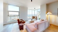 Located in the heart of Seattle, this thoughtfully designed two-bedroom, two-bathroom residence offers a refined urban living experience on a single floor. Light hardwood flooring flows throughout the open layout, anchoring the space with warmth and continuity.

The kitchen is a standout, featuring flat-front cabinetry in a soft blue-grey tone, stainless steel appliances including a French door refrigerator and range, a generous island with a clean stone countertop, and open shelving that adds both function and character. It opens seamlessly toward the living area, where large floor-to-ceiling windows flood the space with natural light and frame impressive views of the Seattle skyline and waterfront.

Both bedrooms are well-proportioned and bright. The primary bedroom includes a dedicated closet, while the second bedroom benefits from a large picture window showcasing sweeping city and water views. Three closets across the residence provide ample storage.

The primary bathroom is elegantly appointed with full-height marble-style tile surrounding a soaking tub, grey stone-look flooring, a wood vanity with a vessel sink, and matte black fixtures. The second bathroom continues the refined aesthetic with warm tile flooring and a tub-shower combination. A dedicated laundry area completes this well-appointed residence.