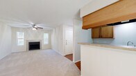 This single-floor, 2-bedroom, 1-bathroom unit offers a well-organized layout across a comfortable footprint. The entrance opens into a hallway that connects the main living areas. The combined kitchen and living room forms the social hub of the unit, where a tile-surround fireplace serves as a focal point flanked by two windows that admit natural light. A ceiling fan is installed overhead, and carpet flooring extends throughout the living area. The galley-style kitchen features warm wood cabinetry, light countertops, black appliances including a refrigerator and electric range, a double sink, and durable wood-look flooring. A pass-through counter connects the kitchen to the living space. Both bedrooms are carpeted and equipped with ceiling fans. The primary bedroom offers a comfortable footprint, while the second bedroom features a window with outdoor tree views, providing a bright atmosphere. The shared bathroom includes a tiled tub-shower surround in neutral stone tones, wood-look flooring, and a classic white fixtures. Throughout the unit, neutral cream-toned walls and consistent finishes create a cohesive, understated aesthetic.