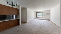 Located at 11800 Eldorado St NW in Coon Rapids, Minnesota, this single-floor, two-bedroom, one-bathroom home offers a practical and straightforward layout across a comfortable footprint. The open living room is a standout feature, highlighted by a large sliding window with wood trim that frames views of surrounding greenery, allowing natural light to fill the carpeted space. A chandelier overhead adds a classic touch, while a baseboard heating system runs along the perimeter. The kitchen sits adjacent to the living area and features warm wood cabinetry with an upper cabinet unit and a built-in counter pass-through, creating a connected feel between the two spaces. Both bedrooms are carpeted and equipped with windows overlooking outdoor greenery, baseboard heaters, and generous closet space—including sliding panel closets. The primary bedroom offers a spacious layout with two separate doorways providing additional flexibility. Throughout the home, consistent wood-trimmed doors, neutral wall tones, and textured ceilings create a cohesive aesthetic. A hallway connects the main living areas to the bedrooms and the full bathroom. Three closets distributed throughout the home offer ample storage for everyday needs.