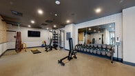 Located at 360 Acoma St in Denver, Colorado, this fitness center offers a comprehensive workout environment spread across a single, generously sized floor. The space is divided into two distinct zones, each thoughtfully designed to support a wide range of fitness activities.

The strength training area features a dark, dramatic ceiling accented by recessed lighting that creates a focused, energetic atmosphere. White subway tile walls add a clean, modern contrast alongside large wall-mounted mirrors that visually expand the space. Equipment includes a multi-station cable machine, adjustable benches, a full rack of dumbbells, a hanging heavy bag for boxing, and a wooden stall bar for functional training. A wall-mounted flat-screen TV completes the area.

The cardio zone is bright and airy, benefiting from floor-to-ceiling windows that frame outdoor views and flood the space with natural light. This section houses treadmills, an elliptical, a stair climber, and a stationary bike equipped with an interactive display. Durable speckled flooring runs throughout both areas, providing a resilient, easy-to-maintain surface suited for high-traffic use.

Together, the two zones create a well-rounded facility that balances functionality with modern design, making it a capable and inviting space for a full spectrum of fitness pursuits.