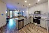 This thoughtfully designed single-floor residence offers a seamless open-concept layout that connects the kitchen, dining, and living areas into one cohesive, light-filled space. The kitchen is a standout feature, showcasing crisp white shaker cabinetry, granite countertops, a subway tile backsplash, and a full suite of stainless steel appliances including a range, microwave, refrigerator, and dishwasher. A peninsula with an undermount sink doubles as a breakfast bar, illuminated by elegant pendant lighting that adds warmth and definition to the space. Wood-style plank flooring flows consistently throughout, lending a clean and contemporary aesthetic. The living area is generously proportioned, with large windows dressed in sheer curtains that invite natural light and provide views to the exterior. A ceiling fan adds comfort and a relaxed ambiance to the room. The bedroom is a serene retreat, featuring its own ceiling fan, a large window, and hardwood-style flooring. The bathroom is well-appointed with granite countertops, white cabinetry, an undermount sink, a walk-in tiled shower, and direct access to a spacious walk-in closet with built-in shelving. Every detail of this residence reflects a modern, polished design sensibility.