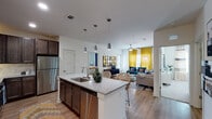 This single-story, 2-bedroom, 2-bathroom residence in Mary Esther, Florida, offers a thoughtfully designed open-concept layout that maximizes functionality and flow. The kitchen serves as a central hub of the living space, featuring dark espresso cabinetry, granite countertops, a subway tile backsplash, stainless steel appliances, and a large island with a built-in sink and seating — illuminated by a row of modern pendant lights. Wood-style flooring extends throughout the main living areas, lending warmth and continuity.

The living room is bright and inviting, benefiting from large windows dressed with bold drapery that allow generous natural light. A ceiling fan adds to the comfort of the space. Both bedrooms are well-proportioned, carpeted for comfort, and include ceiling fans and ample natural light from large windows.

Each of the two bathrooms is finished with granite-topped dark wood vanities, large framed mirrors, and wood-style flooring, maintaining a consistent design language throughout. The overall aesthetic is clean and contemporary, with white walls providing a neutral backdrop that enhances the sense of openness across the entire residence.