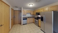 This single-floor residence offers a practical and comfortable layout designed for everyday living. The kitchen is a functional centerpiece, featuring light oak cabinetry, dark granite-style countertops, and a full suite of stainless steel appliances including an electric range, over-the-range microwave, dishwasher, and a side-by-side refrigerator with an in-door ice and water dispenser. Light ceramic tile flooring runs throughout the kitchen, providing easy maintenance and a clean, bright aesthetic. The kitchen flows naturally into an open living area, where neutral-toned carpet begins and the space opens up comfortably. The living area benefits from a sliding glass door that leads to a private balcony, allowing natural light to fill the room. The bedrooms are carpeted and finished with warm-toned wood trim around the windows, each offering views to the outside. The textured ceilings and neutral wall tones carry throughout the unit, lending a cohesive and understated aesthetic. The bathroom is well-appointed with a full-size soaking tub and shower combination, a light wood vanity, tile flooring, and clean white fixtures. Overall, the space presents a straightforward, move-in-ready layout with consistent finishes throughout.
