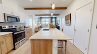 Located at 2500 Bobby Foster Rd SE in Albuquerque, New Mexico, this well-appointed 2-bedroom, 2-bathroom residence offers a thoughtfully designed single-level layout that balances modern aesthetics with Southwest charm. The open-concept kitchen and living area serves as the heart of the home, anchored by a large center island with a white quartz countertop, an integrated sink, and bar seating. Natural wood cabinetry, stainless steel appliances—including a side-by-side refrigerator and range—and a soft tile backsplash complete the kitchen. Exposed wood ceiling beams add warmth and architectural character throughout the main living space, while light wood-tone flooring flows seamlessly underfoot. The living area is bright and inviting, benefiting from a sliding glass door that opens to an outdoor area and allows ample natural light to fill the room. The primary bedroom is generously sized, offering a walk-in closet and a private en-suite bathroom. The second bedroom features a large window with exterior views and light-filled ambiance. Both bathrooms are finished with wood-toned vanities and clean white countertops, maintaining a cohesive, contemporary design throughout. A hallway provides convenient access to all rooms, enhancing the functional flow of the residence.