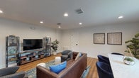 This single-floor lounge is thoughtfully designed to accommodate both relaxed social gatherings and focused work. The space is anchored by warm hardwood flooring throughout and illuminated by recessed ceiling lighting, creating a clean, inviting ambiance. A built-in fireplace serves as a focal point on one wall, flanked by French doors that open to an outdoor area, allowing natural light to filter in and providing a seamless indoor-outdoor connection.

The main seating area features a tufted brown leather sofa and multiple upholstered accent chairs arranged around a colorful area rug, with ceramic garden stools serving as casual side tables. An industrial-style open shelving unit houses a large flat-screen television, books, and decorative accessories, adding both function and visual interest. A lush fiddle-leaf fig plant adds a natural, organic element to the space.

On the opposite end, a dining table surrounded by navy chairs provides a dedicated area for meetings or casual dining, positioned near an arched window that draws in natural light. Curated wall art and decorative accents throughout contribute to the lounge's warm, welcoming character.