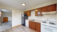 Located at 5479 Scranton Rd in Hamburg, NY, this one-bedroom, one-bathroom unit offers a practical and efficiently laid-out single-floor living space. The kitchen is equipped with warm-toned wooden cabinetry, light countertops, a gas range, dishwasher, and a black refrigerator, all set over light hardwood-style flooring that adds a clean, bright feel to the space. A window above the kitchen provides natural light and outdoor views of surrounding greenery.

The combined living and dining area features plush grey carpeting, neutral cream-toned walls with rich wood trim, and baseboard heating — practical for Hamburg's colder seasons. Multiple windows with wood frames allow natural light to flow in, offering views of the neighborhood.

The bedroom is comfortably proportioned, finished with the same soft carpeting and neutral walls, and benefits from dual windows that bring in additional daylight. It includes two closets with wood-paneled doors, providing ample storage alongside the three total closets found throughout the unit.

The bathroom presents a clean, updated look with a white vanity, full tub-shower combination, and light wood-style flooring that ties cohesively to the rest of the unit. Wood-toned doors and trim are consistent throughout, giving the space a unified, classic aesthetic.