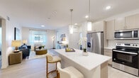 This contemporary single-floor residence offers a thoughtfully designed open-concept layout that seamlessly connects the kitchen, dining, and living areas. The kitchen is a standout feature, boasting light wood cabinetry that extends to the ceiling, stainless steel appliances including a French door refrigerator, a microwave, and a range, complemented by quartz countertops and a subway tile backsplash. A central island with seating for two serves as both a functional workspace and a casual dining spot, illuminated by stylish pendant lighting. The living area flows naturally from the kitchen, featuring light hardwood-style flooring, neutral walls, and large windows dressed with sheer curtains that allow generous natural light to fill the space. The bedrooms are bright and comfortable, each equipped with multiple windows fitted with blinds and sheer drapes, providing both privacy and natural light. The bathroom features a wide vanity with wood cabinetry, a white countertop, and access to a walk-in closet. The attached garage is spacious, fitted with an automatic opener, and benefits from an open view to the outdoors. Throughout the residence, a clean, modern aesthetic is maintained with light tones, contemporary finishes, and cohesive design elements.