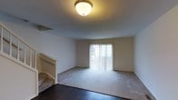 This spacious multi-level residence spans four floors, offering a versatile and expansive layout suited for a variety of living arrangements. The living area features a combination of rich hardwood flooring at the entry and plush carpeting throughout, creating a warm and comfortable atmosphere. A sliding glass door floods the room with natural light while providing direct access to the outdoors, enhancing the sense of openness and connection to the exterior. Neutral-toned walls and understated ceiling fixtures contribute to the clean, move-in-ready aesthetic of the space. A staircase positioned within the living area provides seamless access to the additional floors above, reflecting a practical and well-considered layout. The overall ambiance of the home is bright, airy, and welcoming, with a neutral palette that offers a versatile canvas for personalization. With four floors of living space, this residence provides ample room for both private retreats and shared living, making it a well-appointed home suited to a wide range of needs and lifestyles.