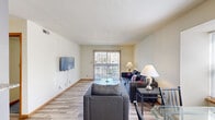 Located at 705 S First St in Champaign, Illinois, this single-floor unit offers a well-organized layout designed for comfortable everyday living. The living room serves as the central gathering space, featuring light wood-look flooring, a wall-mounted flat-screen TV, and a sliding glass door that opens to a private balcony, allowing natural light to fill the room. A dining area is conveniently situated adjacent to the living space, making it easy to entertain or dine at home.

The galley-style kitchen is efficiently designed with warm wood cabinetry, ample overhead storage, a full-size refrigerator, an electric range, a microwave, and a laminate countertop — providing all the essentials for home cooking. Bright overhead lighting ensures the kitchen remains well-lit throughout the day.

Multiple bedrooms are spread throughout the unit, each featuring plush carpeted flooring, ceiling fans, and windows that bring in natural light. The bedrooms include closet storage, making them practical and functional spaces. One bedroom features a built-in closet with shelving, while another offers additional drawer and wardrobe storage.

Overall, the unit presents a clean, neutral aesthetic with light-colored walls and consistent finishes throughout, creating a cohesive and inviting living environment well-suited for residents in the Champaign area.